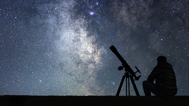 Man sits with telescope looking up at the Milky Way.