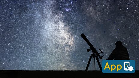 Silhouette of a person sitting beside a telescope on a tripod under a clear night sky filled with dense stars and the bright band of the Milky Way.