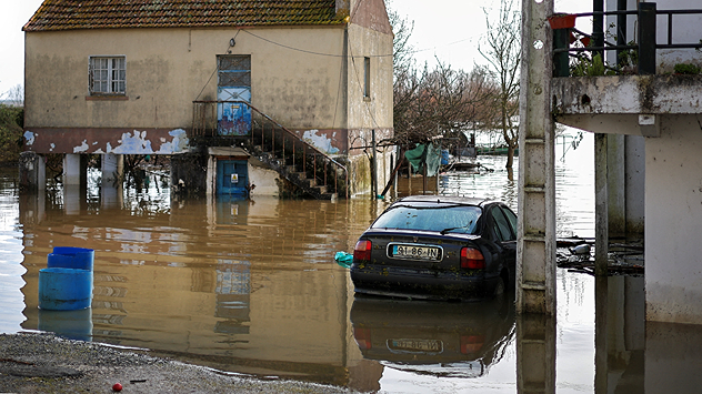 Flooded residential area with half-submerged car Water stands between houses and stairway.